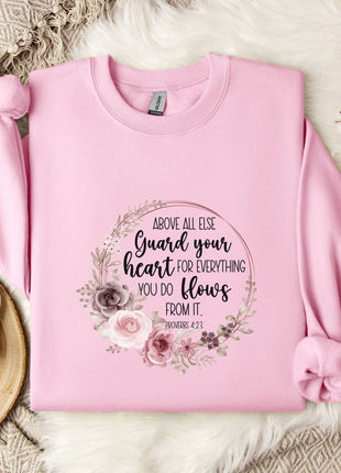 A pink sweatshirt with a floral design and text printed on it, placed on a white fur rug.