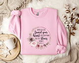 A pink sweatshirt with a floral design and text printed on it, placed on a white fur rug.