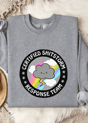 a gray sweatshirt with a graphic design on it, placed on a bed with a blanket and a mug.