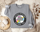 a gray sweatshirt with a graphic design on it, placed on a bed with a blanket and a mug.