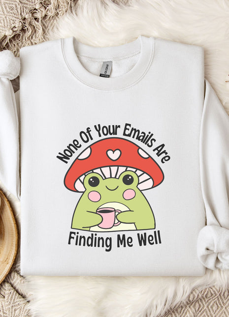 a white sweatshirt with a mushroom-shaped frog graphic and text, along with a mug and a plant on a bed.