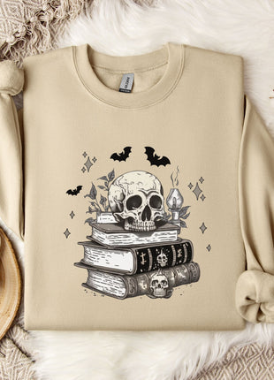 a beige sweatshirt with a skull and bat design on it, along with a stack of books and some white flowers.