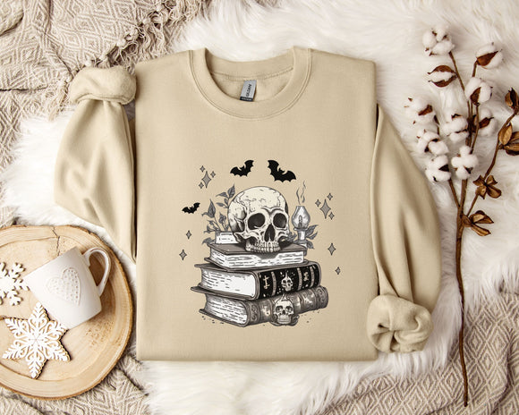a beige sweatshirt with a skull and bat design on it, along with a stack of books and some white flowers.