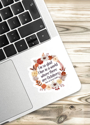 A sticker with a floral design is placed on the edge of a laptop keyboard, resting on a wooden surface.