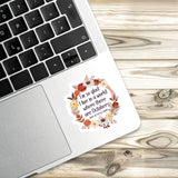 A sticker with a floral design is placed on the edge of a laptop keyboard, resting on a wooden surface.