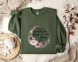 a green sweatshirt with a floral design and text printed on it, along with a mug, a white mug, and some white flowers on a white fur rug.