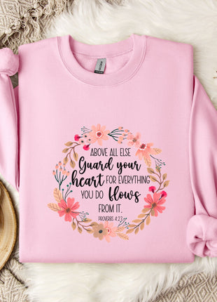 A pink sweatshirt with a floral design and text printed on it, placed on a white fur rug.