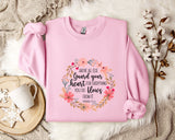 A pink sweatshirt with a floral design and text printed on it, placed on a white fur rug.