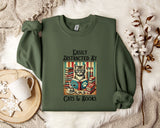 a green sweatshirt with a printed design of a cat surrounded by books and a cup of tea, along with the text "Easily Distracted By Cats & Books".