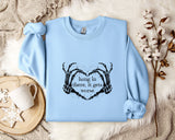 A light blue sweatshirt with a graphic design and text printed on it, along with a mug and some flowers on a bed.