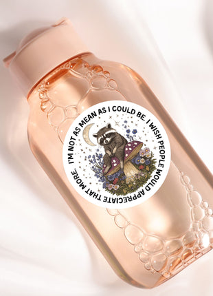 A pink bottle with a sticker featuring a raccoon sitting on a mushroom and surrounded by flowers and mushrooms.