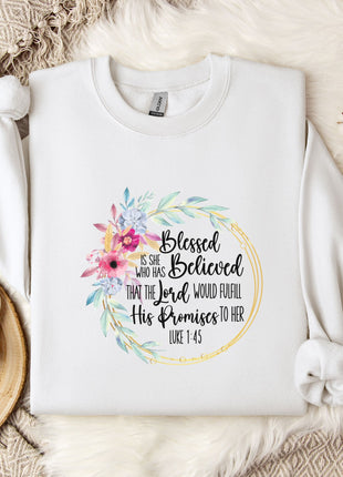 A white t-shirt with a floral design and text printed on it, placed on a bed with a white blanket and a white mug.