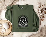 a green sweatshirt with a graphic design on it, placed on a bed with a white blanket and a white mug.