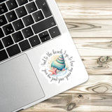 A sticker with a beach scene and a starfish is placed on the edge of a laptop keyboard.