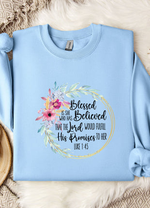 A light blue sweatshirt with a floral design and text printed on it, along with a mug and some white flowers on a bed.