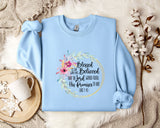 A light blue sweatshirt with a floral design and text printed on it, along with a mug and some white flowers on a bed.