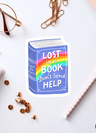 a sticker with the text "Lost in a book don't send help" surrounded by various office supplies such as a pen, a pair of glasses, and a notebook.