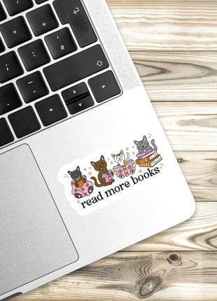 A sticker with a cartoon image of three cats and the text "read more books" is placed on the edge of a laptop keyboard.
