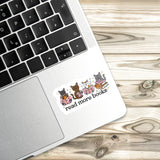 A sticker with a cartoon image of three cats and the text "read more books" is placed on the edge of a laptop keyboard.