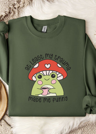 A green sweatshirt with a mushroom graphic and text, along with a mug and a white flower, placed on a white fur rug.