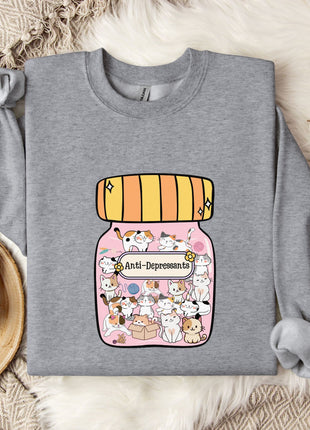 A gray sweatshirt with a graphic of a jar containing cats and the text "Anti-Depressants" printed on it, along with a mug and some flowers on a bed.