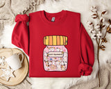 A red sweater with a cartoon illustration of a jar filled with cats and the text "Anti-Depressants" printed on it, placed on a white fur rug.