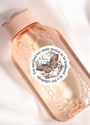 A pink bottle with a label featuring a butterfly and the text "I survive too many storms to be a butterfly"