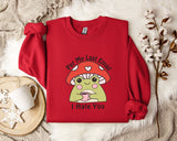 a red sweater with a cartoon frog wearing a red hat and holding a cup, accompanied by a mug and a white flower on a white fur rug.