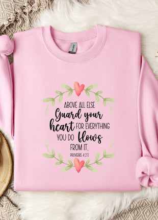 A pink sweatshirt with a printed Bible verse and a floral wreath design, along with a mug and a branch of cotton bolls, all placed on a white fur rug.