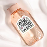 A pink bottle with a label that says "The grass is greener where you water it" and features a butterfly and a watering can.