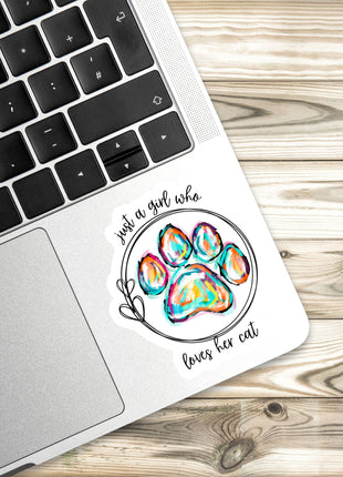 A sticker with a paw print and the text "Just a girl who loves her cat" is placed on a laptop keyboard.