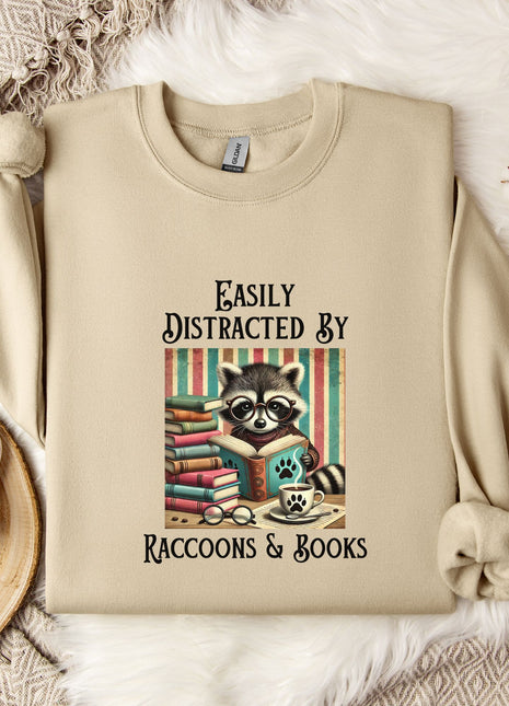 a beige sweatshirt with a raccoon graphic and text, along with a mug, a plant, and some cotton balls, all arranged on a white fur rug.