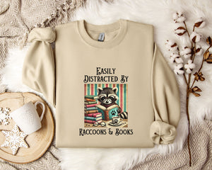 a beige sweatshirt with a raccoon graphic and text, along with a mug, a plant, and some cotton balls, all arranged on a white fur rug.