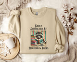 a beige sweatshirt with a raccoon graphic and text, along with a mug, a plant, and some cotton balls, all arranged on a white fur rug.