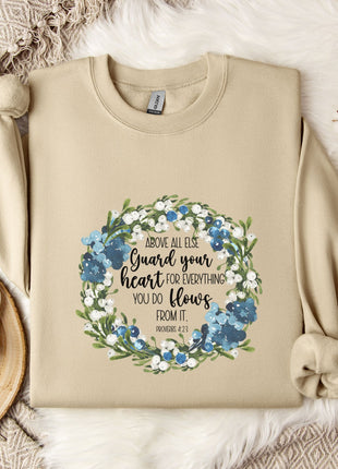 A beige sweatshirt with a floral design and text printed on it, along with a mug, a branch of cotton flowers, and a wooden tray with snowflakes on it, all arranged on a white fur rug.