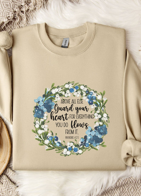 A beige sweatshirt with a floral design and text printed on it, along with a mug, a branch of cotton flowers, and a wooden tray with snowflakes on it, all arranged on a white fur rug.