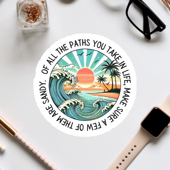 A sticker with a beach scene and a sunset, surrounded by various office supplies and a pair of glasses on a white surface.