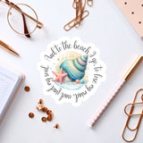 a sticker with a seashell and starfish design, surrounded by various office supplies such as pens, paper clips, and a pair of glasses.