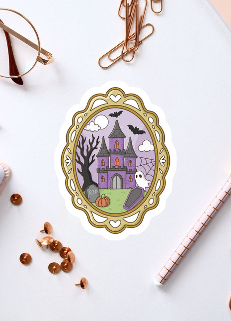 a sticker of a castle with a ghost, surrounded by various office supplies such as a pen, a notebook, and a pair of glasses.