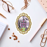 a sticker of a castle with a ghost, surrounded by various office supplies such as a pen, a notebook, and a pair of glasses.