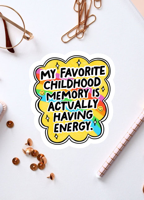 a sticker with a colorful design and text, surrounded by various office supplies such as a pen, a pair of glasses, and a notebook.