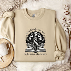 a beige sweatshirt with a graphic design on it, along with a mug, a plant, and some flowers on a bed.