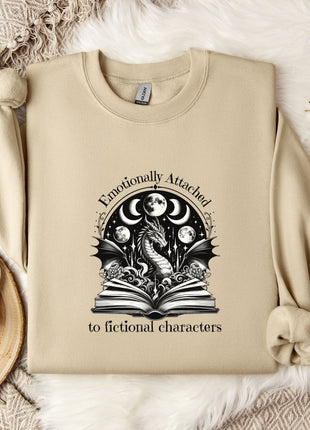 a beige sweatshirt with a graphic design on it, along with a mug, a plant, and some flowers on a bed.