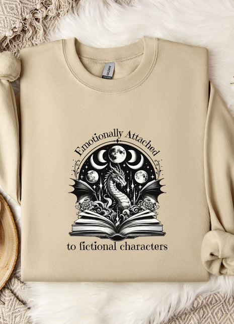 a beige sweatshirt with a graphic design on it, along with a mug, a plant, and some flowers on a bed.