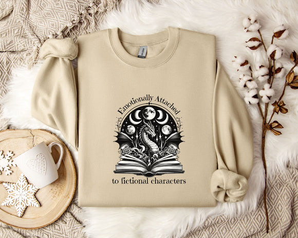 a beige sweatshirt with a graphic design on it, along with a mug, a plant, and some flowers on a bed.