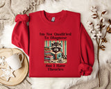 A red sweatshirt with a graphic design of a raccoon reading a book, accompanied by text that reads "I'm Not Qualified To Diagnose But I Have Theories".