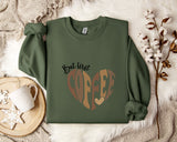 a green sweatshirt with a heart-shaped design and the text "But first coffee" printed on it, along with a mug and some flowers.
