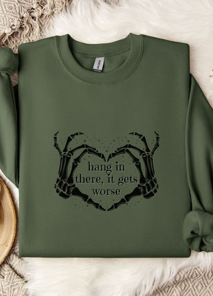 A green sweatshirt with a graphic design and text printed on it, along with a mug and some white flowers on a white surface.