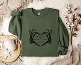 A green sweatshirt with a graphic design and text printed on it, along with a mug and some white flowers on a white surface.