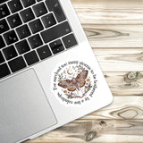 A sticker with a butterfly and floral design is placed on the edge of a laptop keyboard.